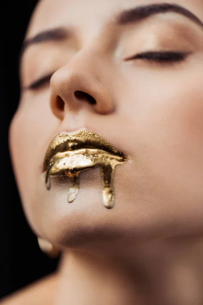 Close up de jovem mulher com olhos fechados e lábios pintados de ouro isolado em preto — Fotografia de Stock