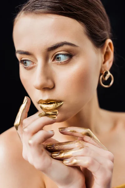 Mujer desnuda joven con maquillaje dorado y pintura dorada en los dedos aislados en negro - foto de stock