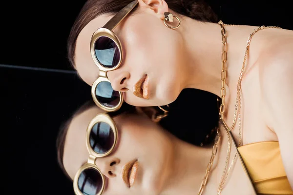 Молода жінка в сонцезахисних окулярах, золоті намиста тримають дзеркало ізольовано на чорному — стокове фото