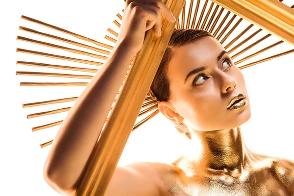 Nude young woman painted in golden with accessory on head looking away and holding frame isolated on white — Stock Photo