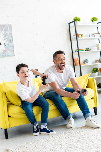 Excited father and son playing Video Game on couch in Living Room — Stock Photo