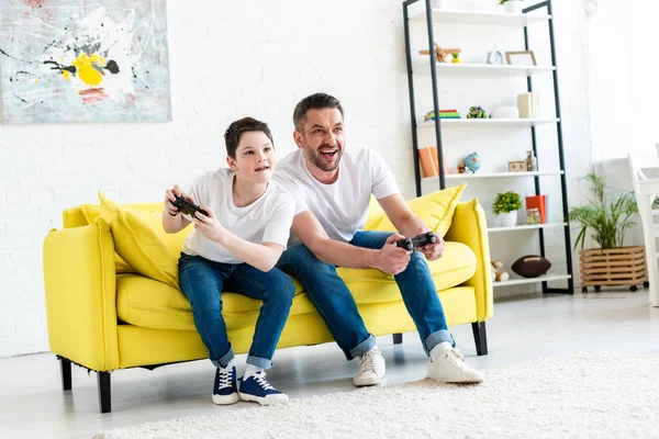 Vater und Sohn mit Steuerknüppeln spielen Videospiel auf Couch im Wohnzimmer — Stockfoto