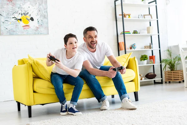 Father and son with joysticks playing Video Game on couch in Living Room — Stock Photo