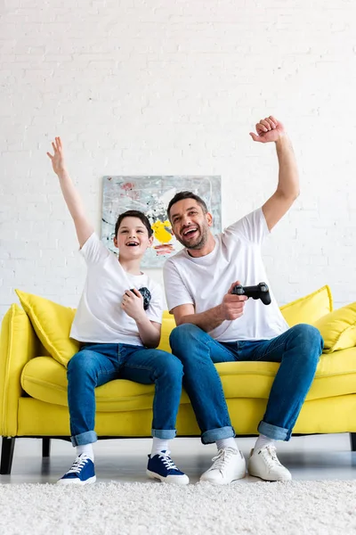 Pai e filho aplaudindo enquanto joga Video Game no sofá em casa — Fotografia de Stock