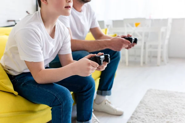 Vue recadrée du père et du fils jouant au jeu vidéo sur le canapé dans le salon — Photo de stock