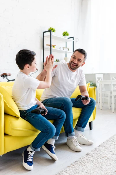 Padre e figlio fare alto cinque gesto durante la riproduzione di videogiochi sul divano a casa — Foto stock