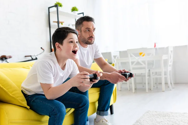 Padre e figlio che giocano a videogame sul divano in salotto con spazio copia — Foto stock