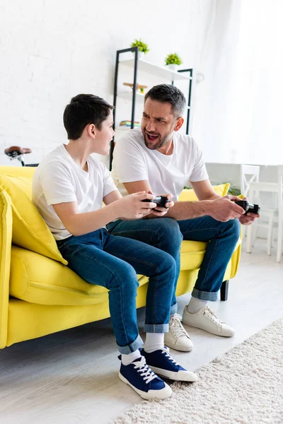 Excited father and son playing Video Game while sitting on couch in Living Room — Stock Photo