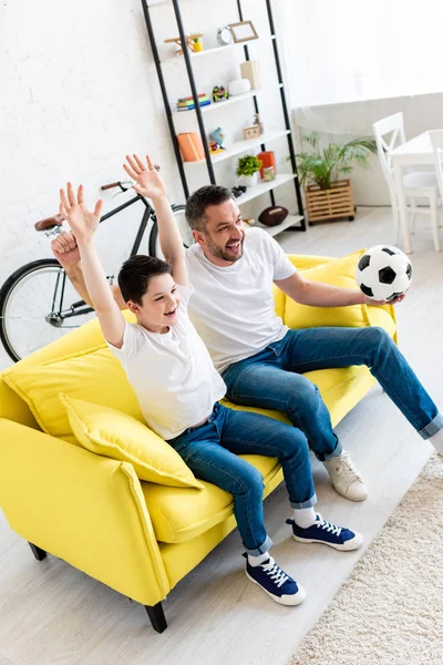 Animado pai e filho no sofá assistindo jogo de esportes e torcendo na sala de estar — Fotografia de Stock