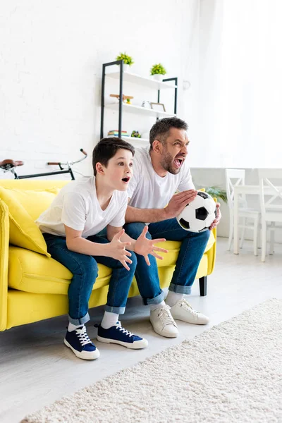 Animado pai e filho assistindo jogo de esportes no sofá em casa — Fotografia de Stock