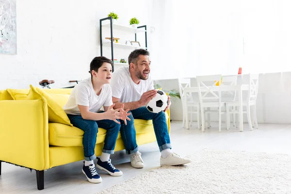 Збуджений батько і син дивиться спортивний матч на дивані вдома з копіювальним простором — стокове фото