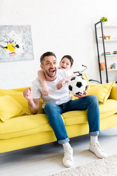 Збуджений батько і син дивляться спортивні матчі і оплески у вітальні — стокове фото