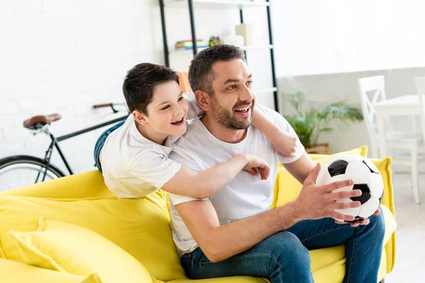 Glücklicher Vater und Sohn beim Sportspiel auf der Couch mit Fußballball zu Hause — Stockfoto