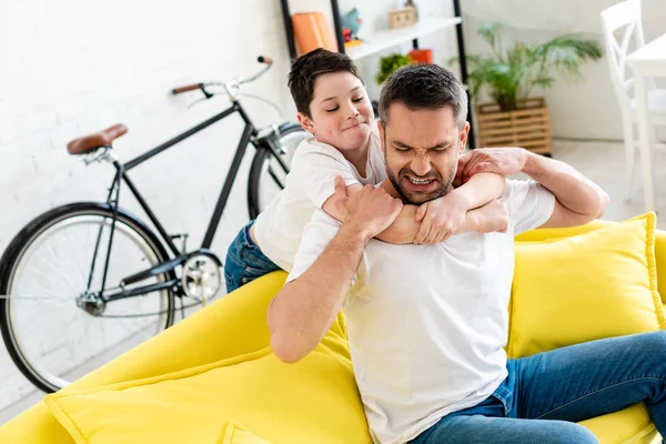 Figlio abbracciare padre irritato seduto sul divano a casa — Foto stock