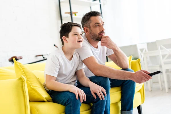 Father and son sitting on couch and watching tv at home — Stock Photo