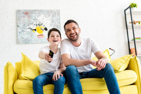 Happy father and son sitting on couch and watching tv at home — Stock Photo