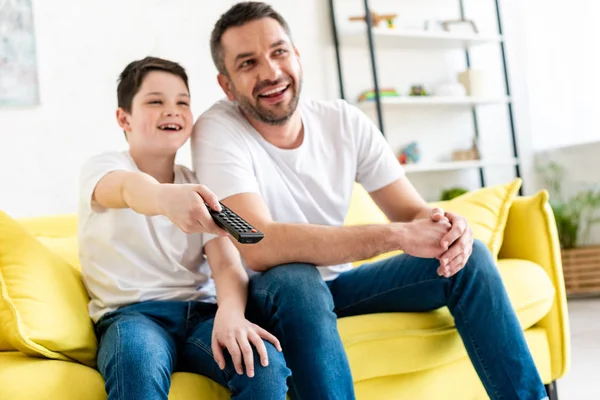 Foco seletivo de pai e filho feliz sentado no sofá e assistindo tv em casa — Fotografia de Stock