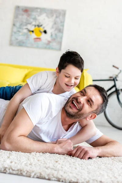Glücklicher Vater und Sohn liegen auf Teppich und umarmen sich zu Hause — Stockfoto