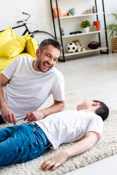 Schöner Vater lacht und sieht Sohn zu Hause auf Teppich liegen — Stockfoto