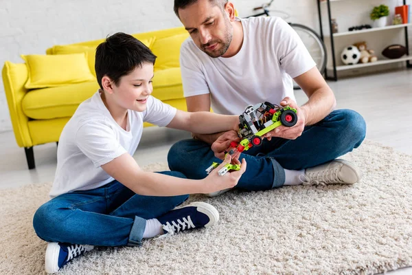 Отец и сын сидят на ковре и играют с игрушечной машиной дома — стоковое фото