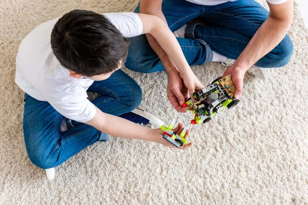 Vista superior del padre y el hijo sentados en la alfombra y jugando con el coche de juguete en casa - foto de stock