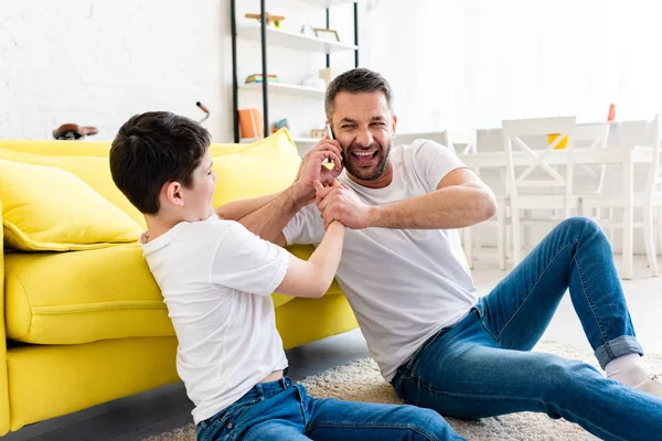 Hijo quitando teléfono inteligente de padre en la sala de estar - foto de stock