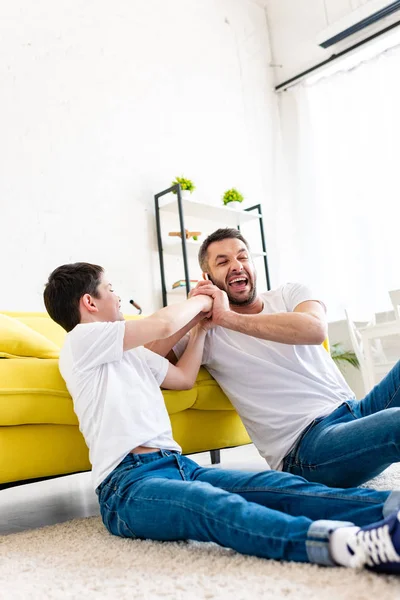 Filho levando smartphone de rir pai na sala de estar — Fotografia de Stock