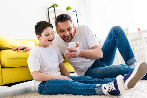 Felice padre e figlio utilizzando lo smartphone in salotto — Foto stock