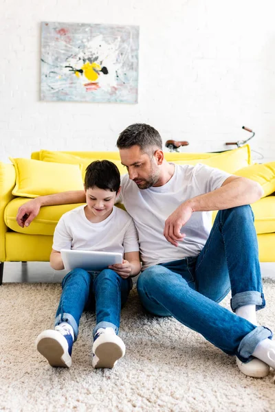 Padre e hijo sentado en la alfombra y el uso de la tableta digital en la sala de estar - foto de stock