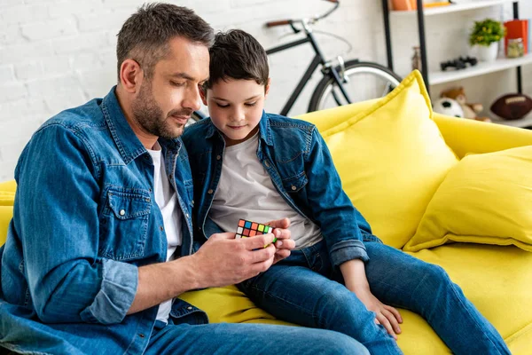 Father and son sitting on couch and playing with toy cube at home — Stock Photo