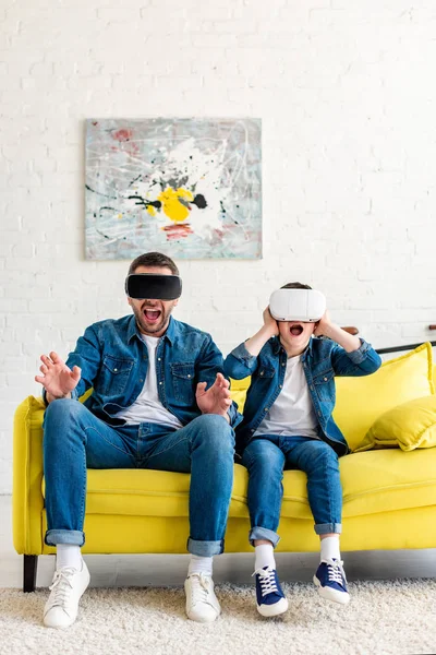 Shocked father and son in vr headsets experiencing Virtual reality on couch at home — Stock Photo