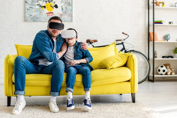 Frightened father and son in vr headsets experiencing Virtual reality on couch at home — Stock Photo