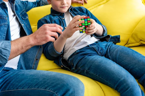Vista recortada de padre e hijo sentado en el sofá y jugando con cubo de juguete en casa - foto de stock