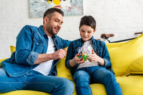 Father and son sitting on couch and playing with toy cube at home — Stock Photo