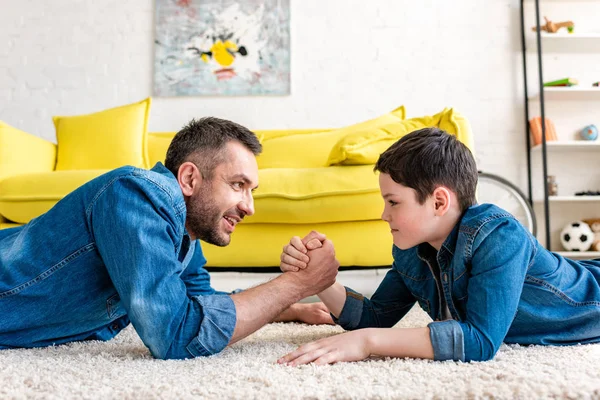 Pai e filho deitado no tapete e braço lutando em casa na sala de estar — Fotografia de Stock