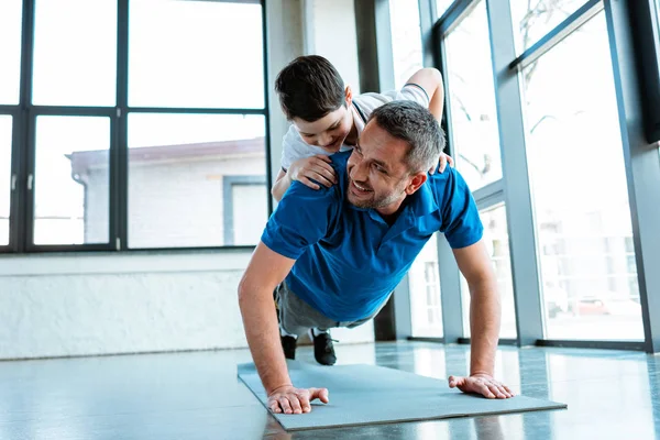 Padre feliz haciendo ejercicio push up con el hijo en la espalda en el gimnasio con espacio de copia - foto de stock