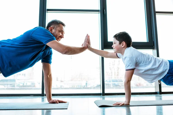 Father and son doing high five sign while doing push up exercise at gym — Stock Photo