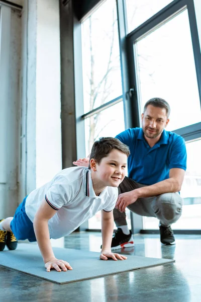 Pai ajudando filho com empurrar para cima exercício no ginásio — Fotografia de Stock