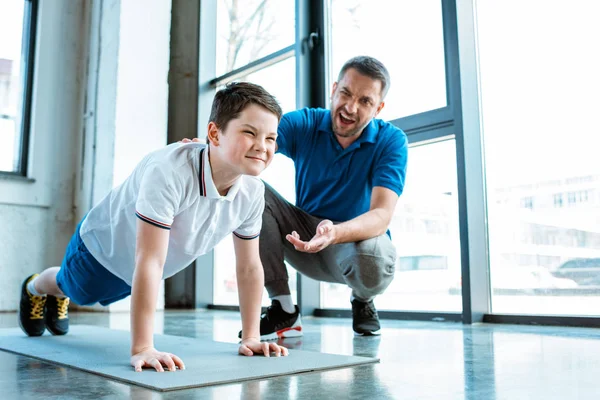 Pai ajudando filho com empurrar para cima exercício no ginásio — Fotografia de Stock