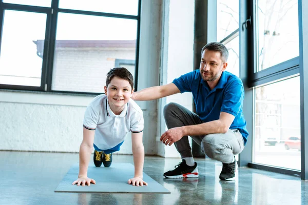 Padre che aiuta il figlio sorridente con l'esercizio di tavola in palestra — Foto stock