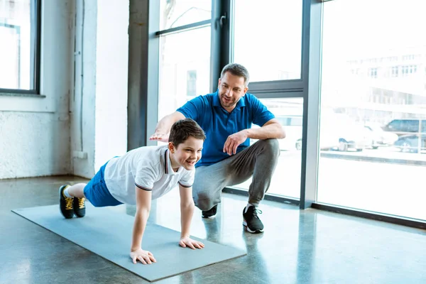 Padre ayudando a su hijo con el ejercicio push up en el gimnasio con espacio de copia - foto de stock