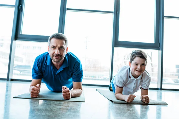 Padre e hijo haciendo ejercicio de tablón en colchonetas de fitness en el gimnasio - foto de stock