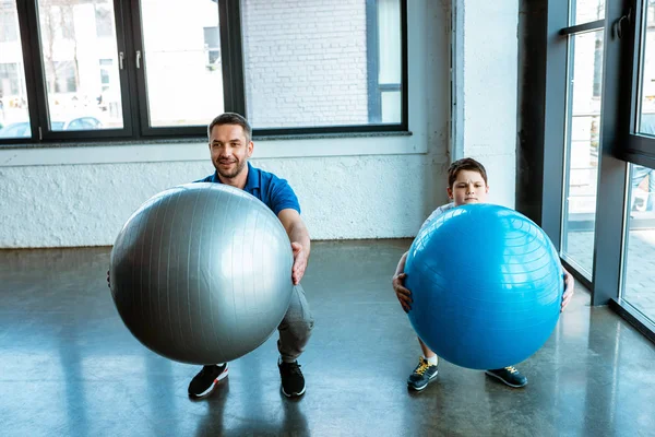 Отец и сын делают приседания с фитнес-мячами в тренажерном зале — стоковое фото