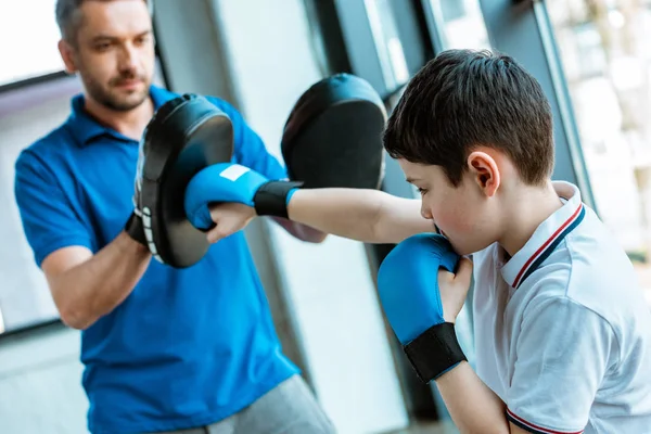 Enfoque selectivo del hijo en el entrenamiento de guantes de boxeo con el padre en el gimnasio - foto de stock
