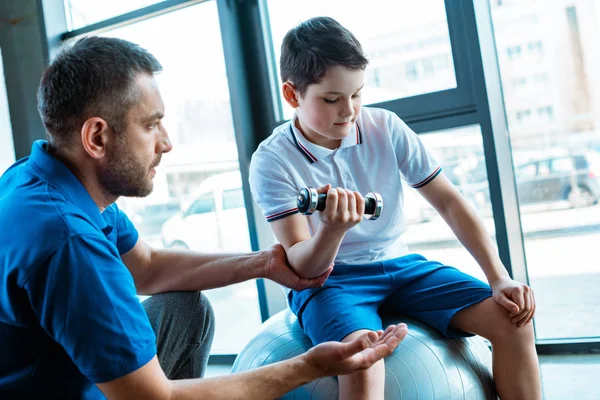 Handsome father helping son exercising with dumbbell at gym — Stock Photo