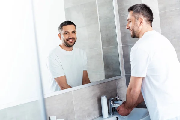 Красивий усміхнений чоловік миє руки у ванній під час ранкової рутини — стокове фото