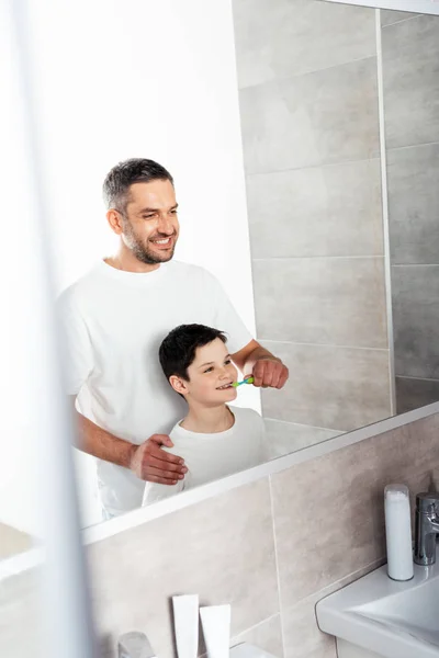Padre cepillarse los dientes del hijo en el baño durante la rutina de la mañana - foto de stock