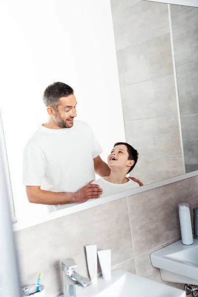 Красивый отец обнимает сына в ванной комнате во время утренней рутины — стоковое фото