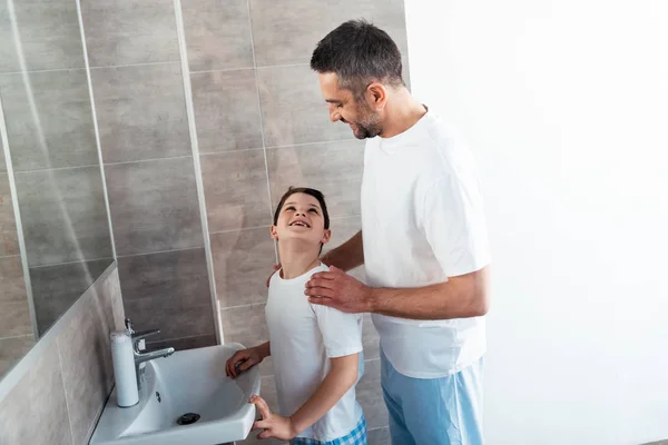 Отец обнимает улыбающегося сына в ванной во время утренней рутины — стоковое фото