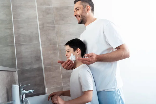 Батько наносить крем для гоління на обличчя сина у ванній — стокове фото